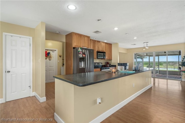 kitchen with appliances with stainless steel finishes, dark countertops, light wood-style flooring, and brown cabinets