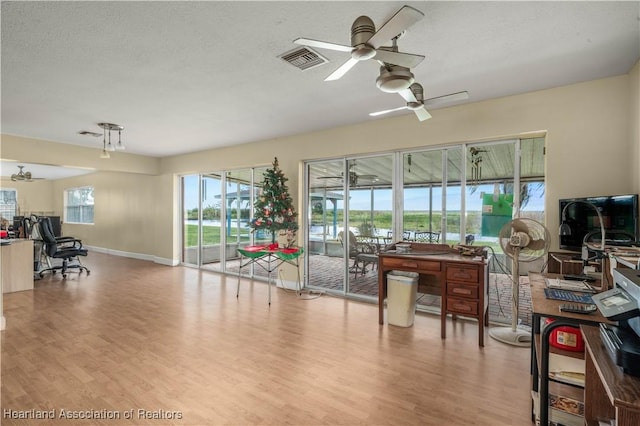 living room featuring visible vents, light wood finished floors, a textured ceiling, and a ceiling fan