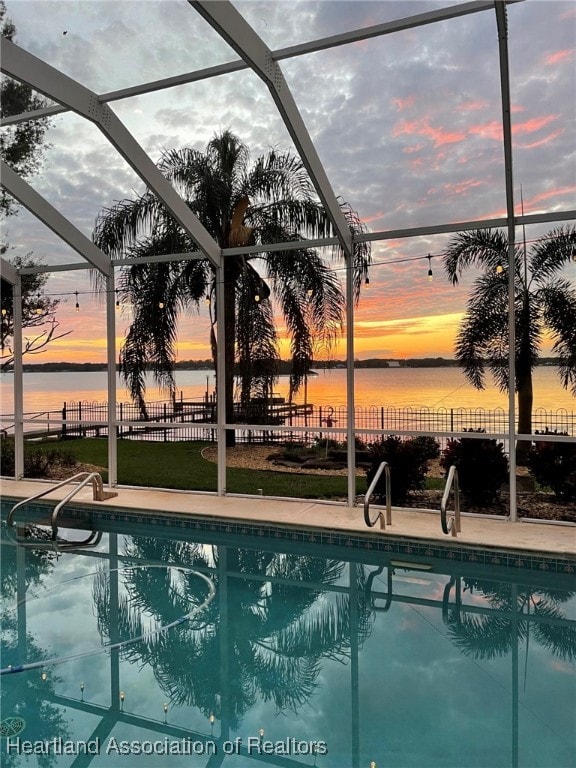 pool at dusk featuring a lanai and a water view