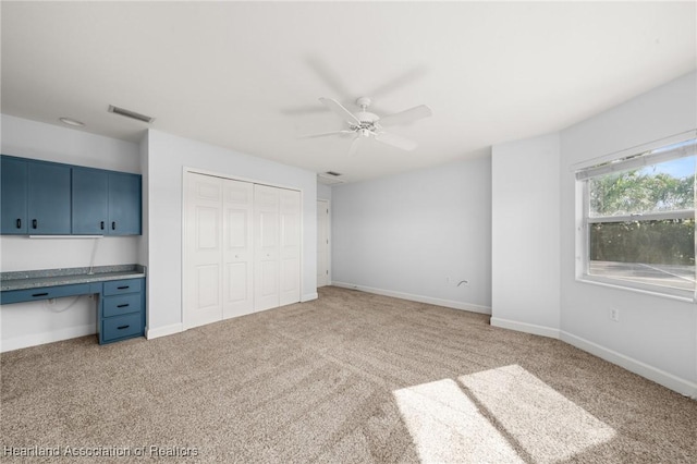 unfurnished bedroom with ceiling fan, light colored carpet, a closet, and built in desk