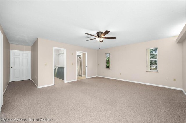 unfurnished bedroom with multiple windows, a walk in closet, a closet, and ceiling fan