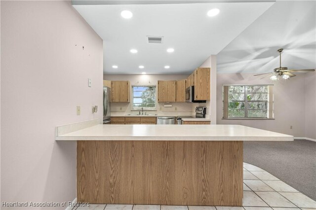 kitchen featuring a healthy amount of sunlight, light colored carpet, kitchen peninsula, and stainless steel appliances