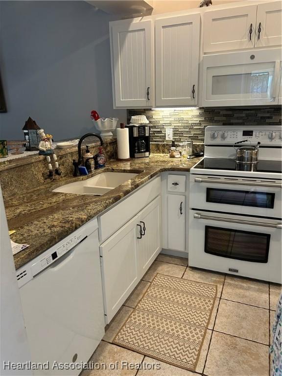 kitchen with white appliances, dark stone counters, a sink, white cabinetry, and backsplash