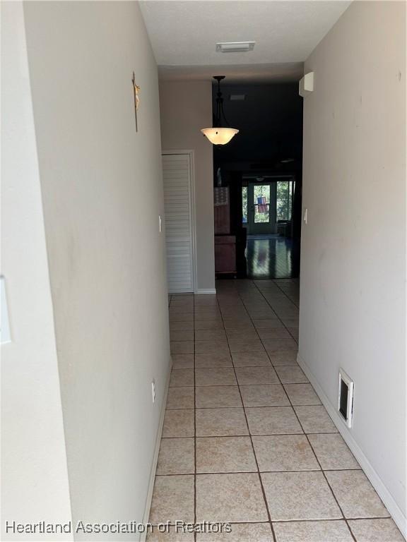 hall with light tile patterned floors, visible vents, and baseboards