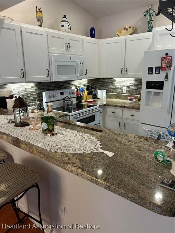 kitchen with white appliances, dark stone countertops, white cabinets, and backsplash