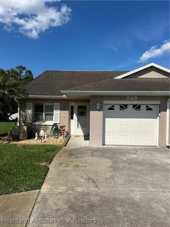 ranch-style home with a shingled roof, concrete driveway, an attached garage, and stucco siding