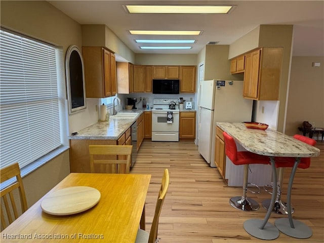 kitchen with white appliances, sink, light hardwood / wood-style flooring, a skylight, and light stone countertops