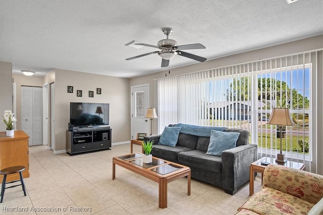 living room featuring light tile patterned floors, a ceiling fan, baseboards, and a textured ceiling