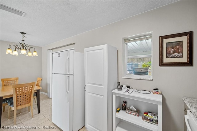 kitchen with visible vents, a textured ceiling, freestanding refrigerator, light tile patterned floors, and a chandelier