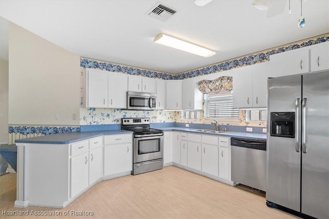 kitchen with sink, white cabinets, stainless steel appliances, and light hardwood / wood-style floors