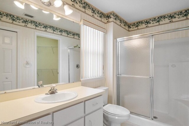 bathroom featuring a shower with door, vanity, and toilet