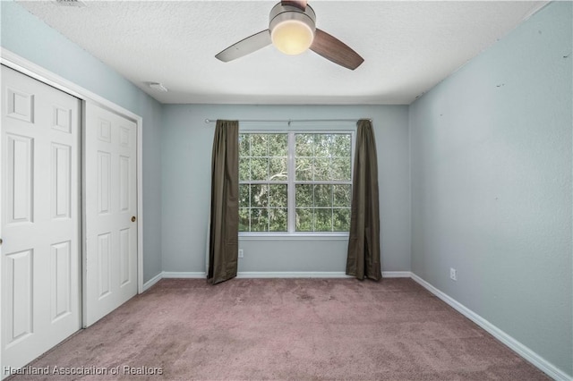 unfurnished bedroom featuring ceiling fan, light colored carpet, a textured ceiling, and a closet