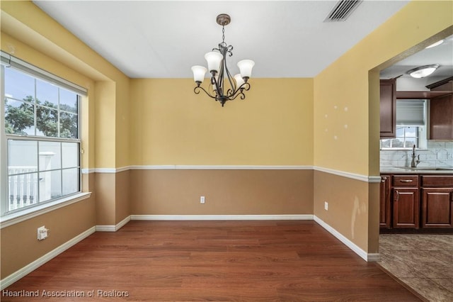 unfurnished dining area featuring sink, dark wood-type flooring, and an inviting chandelier