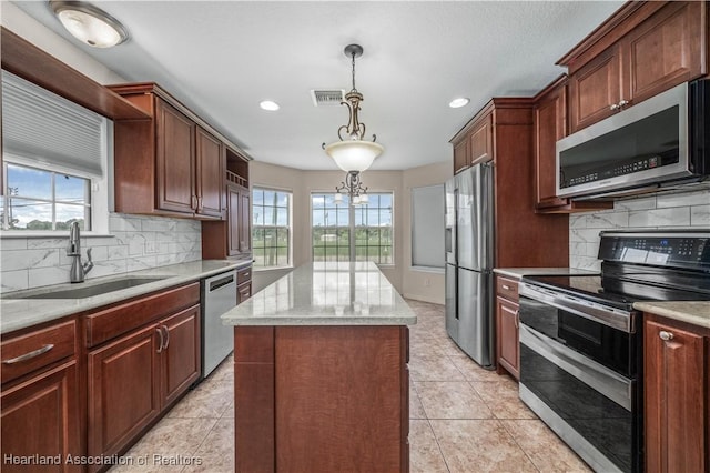 kitchen with appliances with stainless steel finishes, a healthy amount of sunlight, sink, pendant lighting, and a kitchen island