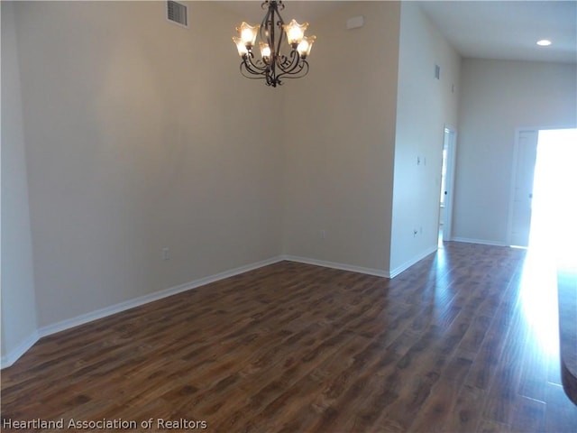 spare room with a towering ceiling, dark hardwood / wood-style flooring, and an inviting chandelier