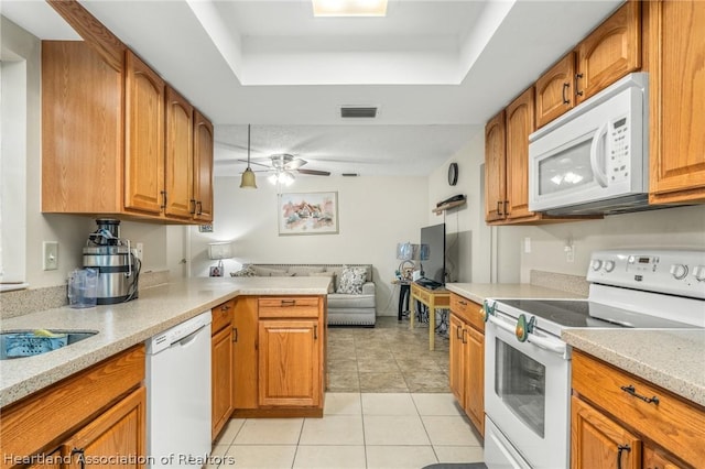 kitchen featuring white appliances, ceiling fan, light tile patterned floors, a tray ceiling, and kitchen peninsula