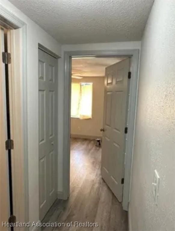 hallway with light hardwood / wood-style flooring and a textured ceiling