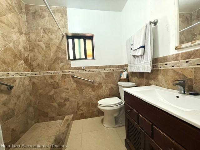 bathroom featuring toilet, tile walls, a tile shower, vanity, and tile patterned flooring