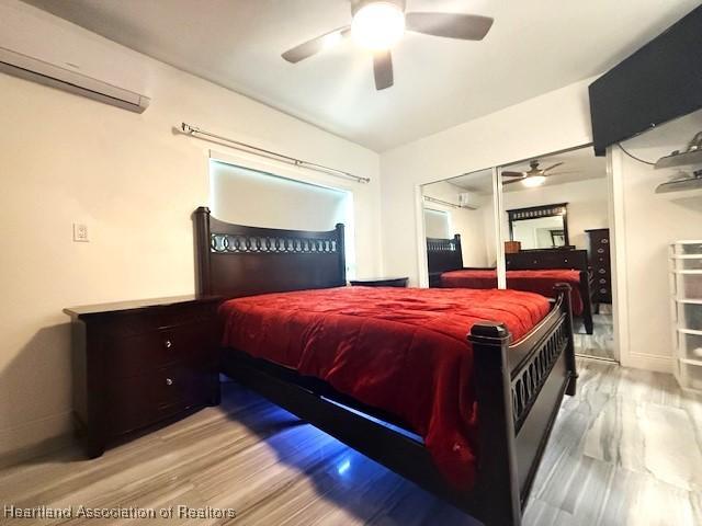 bedroom featuring light wood-type flooring, a wall mounted air conditioner, and ceiling fan