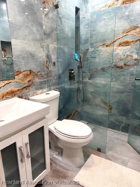 bathroom featuring tile patterned floors, toilet, tile walls, a tile shower, and vanity