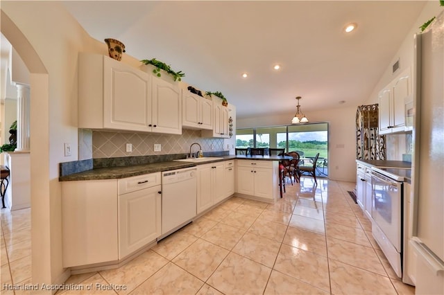 kitchen with white appliances, backsplash, dark countertops, arched walkways, and a peninsula