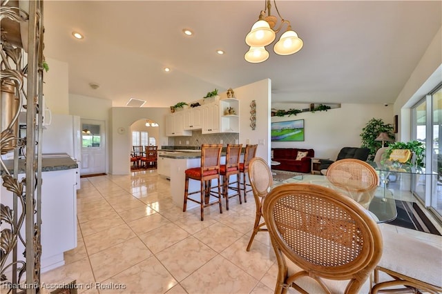 dining area with light tile patterned floors, arched walkways, lofted ceiling, and recessed lighting