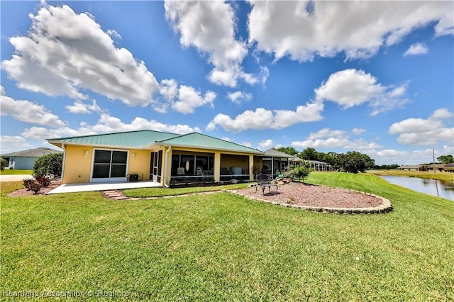 rear view of house featuring a sunroom, stucco siding, metal roof, a water view, and a yard