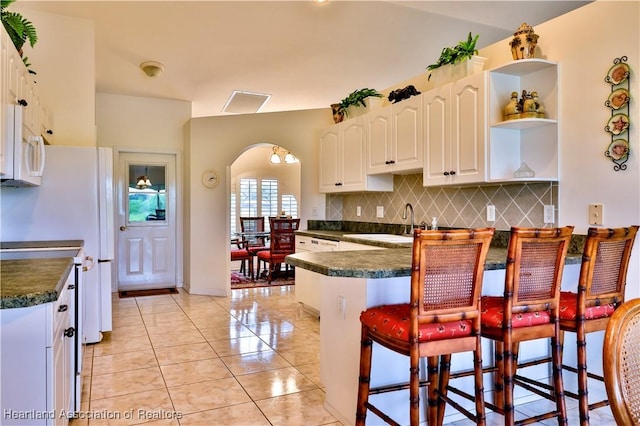 kitchen featuring white cabinets, dark countertops, a peninsula, a kitchen bar, and open shelves