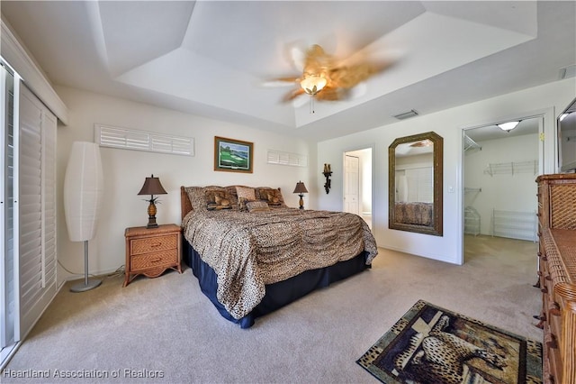 bedroom with a raised ceiling, light carpet, a closet, and visible vents