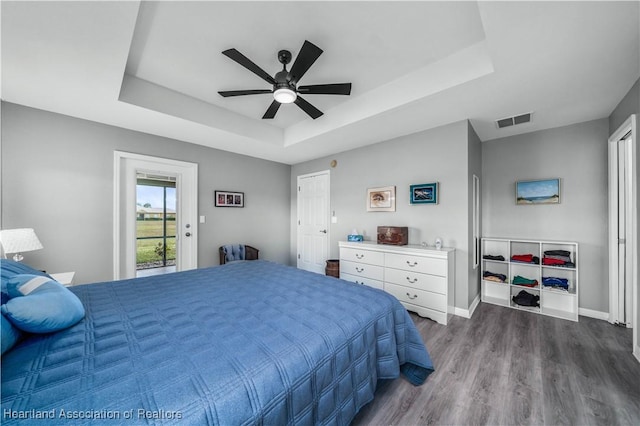 bedroom featuring access to exterior, a tray ceiling, ceiling fan, and dark wood-type flooring