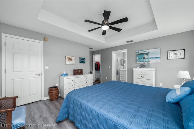 bedroom with hardwood / wood-style floors, ceiling fan, connected bathroom, and a tray ceiling