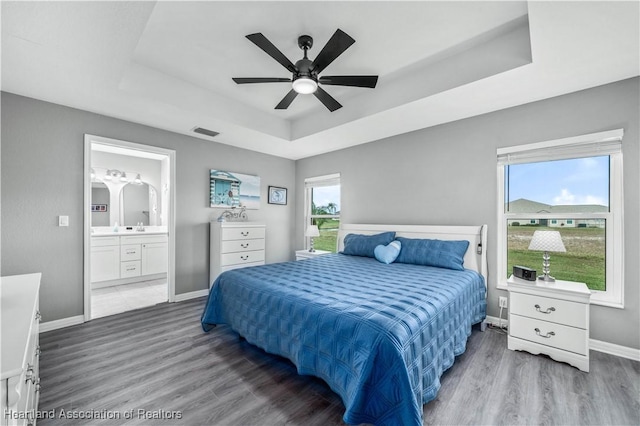 bedroom with wood-type flooring, ensuite bathroom, a raised ceiling, and ceiling fan