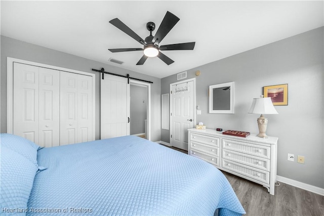 bedroom with ceiling fan, a barn door, dark wood-type flooring, and a closet