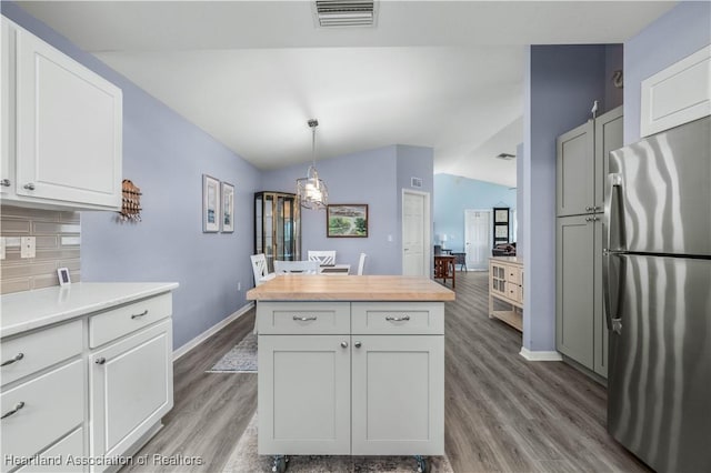 kitchen featuring stainless steel fridge, backsplash, white cabinetry, hanging light fixtures, and lofted ceiling