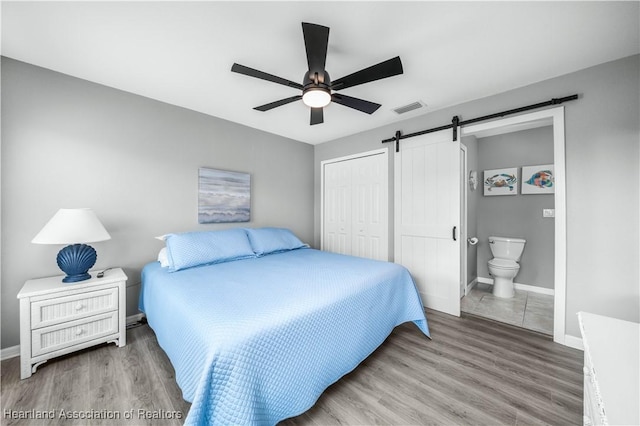 bedroom featuring ensuite bath, hardwood / wood-style flooring, ceiling fan, a barn door, and a closet