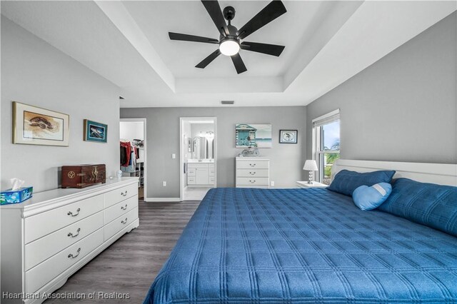 bedroom featuring a raised ceiling, a walk in closet, ensuite bath, ceiling fan, and dark hardwood / wood-style floors