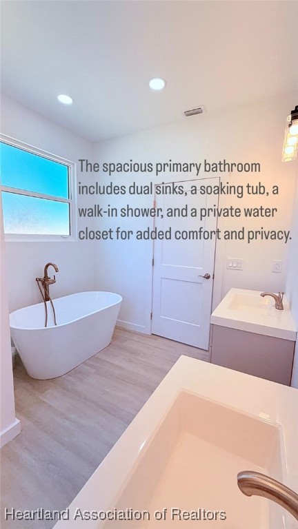 full bathroom featuring recessed lighting, a freestanding tub, and wood finished floors