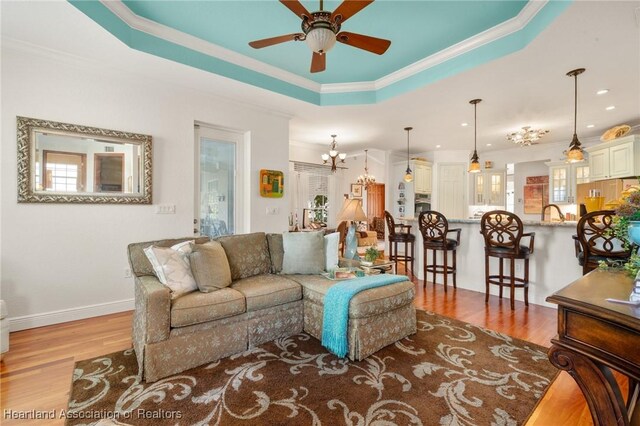 living room with crown molding, a tray ceiling, ceiling fan with notable chandelier, and light hardwood / wood-style floors