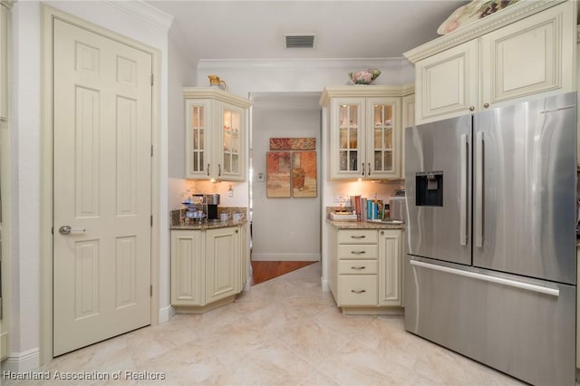 kitchen with stone counters, ornamental molding, stainless steel fridge, and cream cabinetry