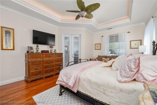 bedroom featuring light hardwood / wood-style flooring, ornamental molding, ceiling fan, a raised ceiling, and french doors