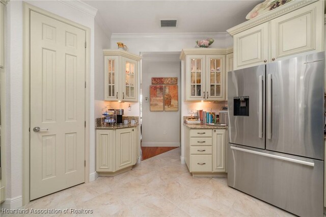 kitchen with cream cabinets, ornamental molding, stone counters, and stainless steel refrigerator with ice dispenser