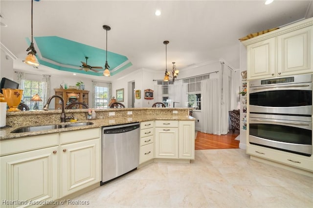 kitchen featuring appliances with stainless steel finishes, decorative light fixtures, sink, light stone counters, and cream cabinets