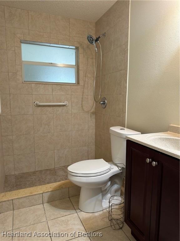 bathroom featuring toilet, vanity, a tile shower, and tile patterned flooring