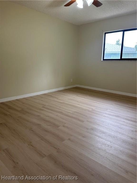 unfurnished room with ceiling fan, a textured ceiling, and light wood-type flooring