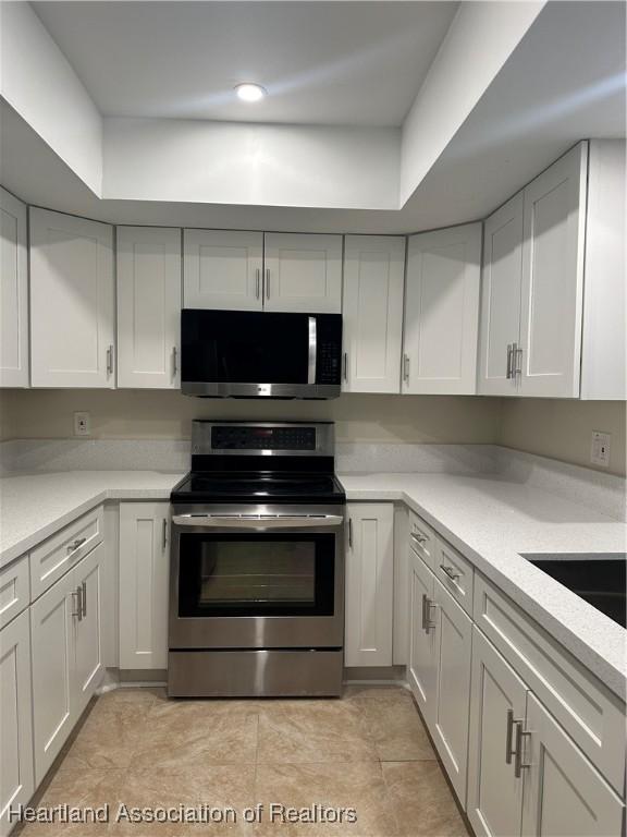 kitchen with light stone countertops, white cabinetry, appliances with stainless steel finishes, and light tile patterned flooring