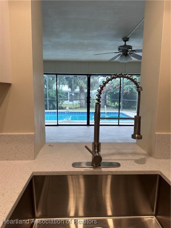 kitchen with ceiling fan, light stone countertops, and sink