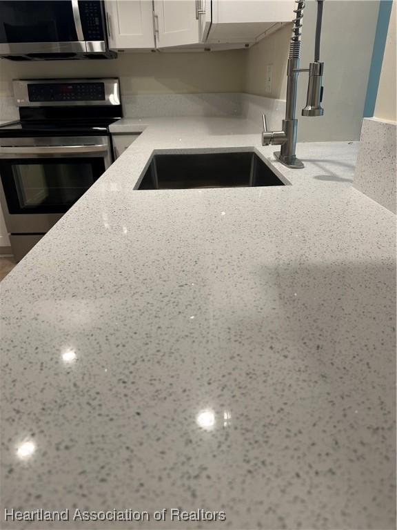 kitchen featuring stainless steel appliances, sink, white cabinetry, and light stone countertops