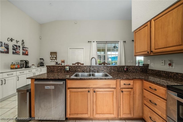 kitchen featuring stainless steel dishwasher, light tile patterned flooring, sink, and dark stone counters