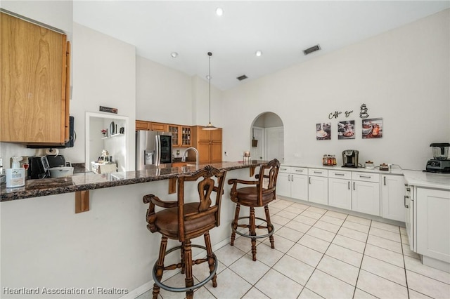 kitchen with white cabinetry, stainless steel refrigerator with ice dispenser, dark stone countertops, a breakfast bar, and light tile patterned flooring