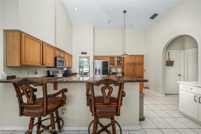 kitchen featuring dark stone counters, hanging light fixtures, stainless steel appliances, and a kitchen breakfast bar